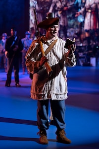 An Army soldier dressed in a colonial-style costume is holding a book in his had while delivering a monologue.