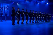Army Soldiers in dark ceremonial uniforms are standing in a straight line doing various movements with their ceremonial rifles.