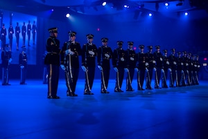 Army Soldiers in dark ceremonial uniforms are standing in a straight line doing various movements with their ceremonial rifles.