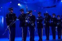 Army Soldiers in dark ceremonial uniforms are twirling ceremonial rifles, and some rifles have been tossed into the air for others to catch.