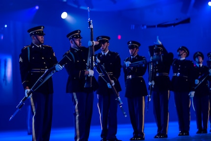 Army Soldiers in dark ceremonial uniforms are twirling ceremonial rifles, and some rifles have been tossed into the air for others to catch.