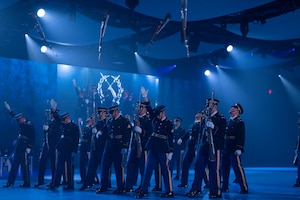 Army Soldiers in dark ceremonial uniforms are marching with ceremonial rifles, and some rifles have been tossed into the air for others to catch.