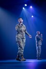 Two Soldiers in Army Combat Uniforms are holding microphones and singing on a stage during a ceremony.