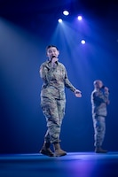 Two Soldiers in Army Combat Uniforms are holding microphones and singing on a stage during a ceremony.