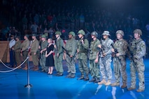 About a dozen Soldiers dressed in various Army uniforms and outfits are standing in a straight line facing the left side of the picture.