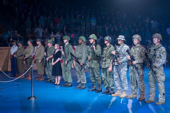 About a dozen Soldiers dressed in various Army uniforms and outfits are standing in a straight line facing the left side of the picture.