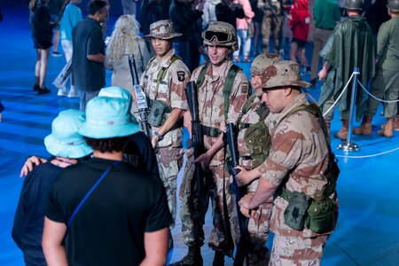 Soldiers in Army Combat Uniforms (green camouflage) are talking with younger audience member after a ceremony. The audience members are each wearing black shirts and mint green hats.