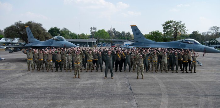 Airman 1st Class Darren Ky, left, and Senior Airman Ashley Taylor, both 80th Fighter Generation Squadron aircraft armament systems, perform a gesture of squadron pride while transitting to conduct maintenance on an F-16 Fighting Falcon