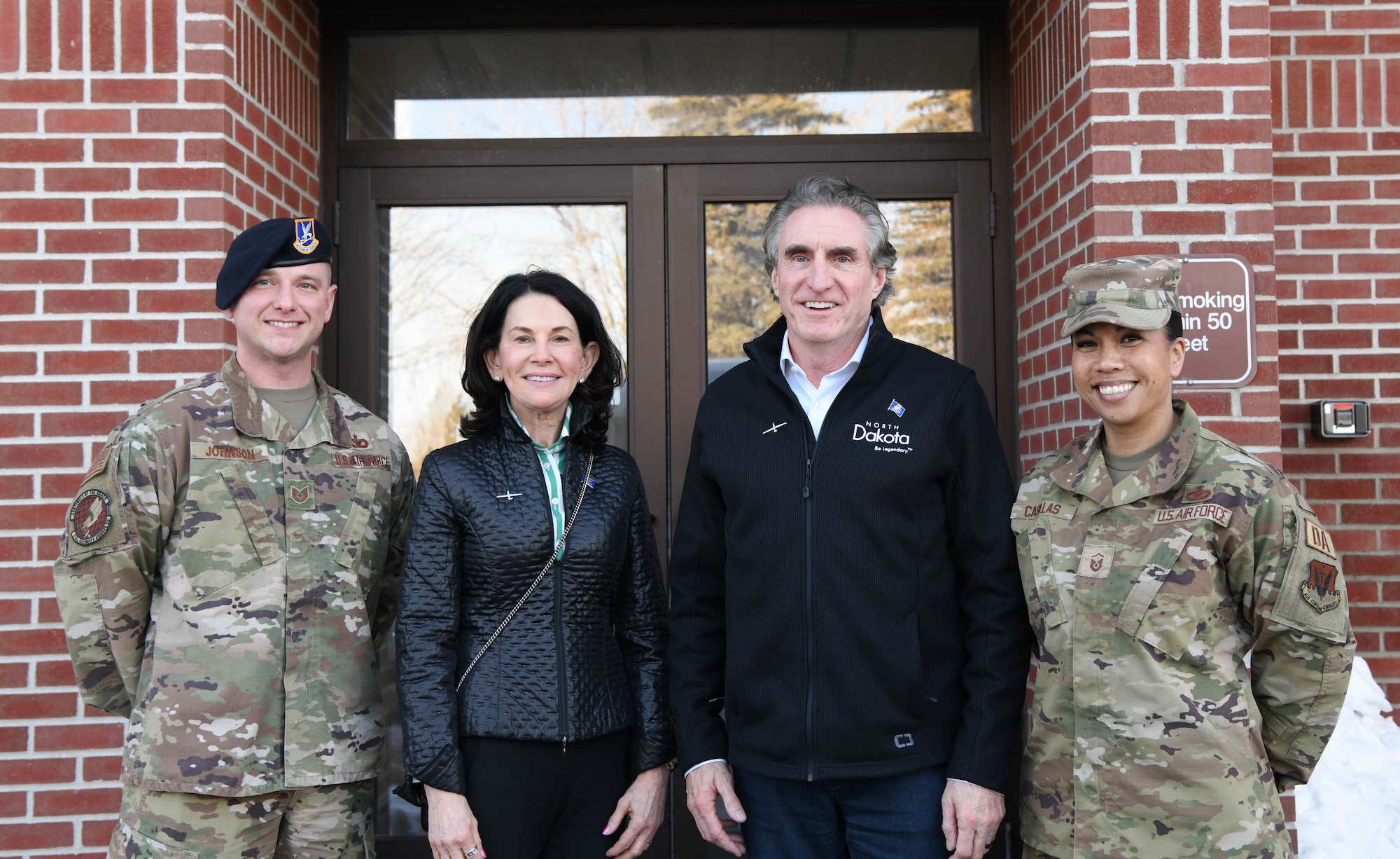 Two military members pose for a photo with two others in front of a building.
