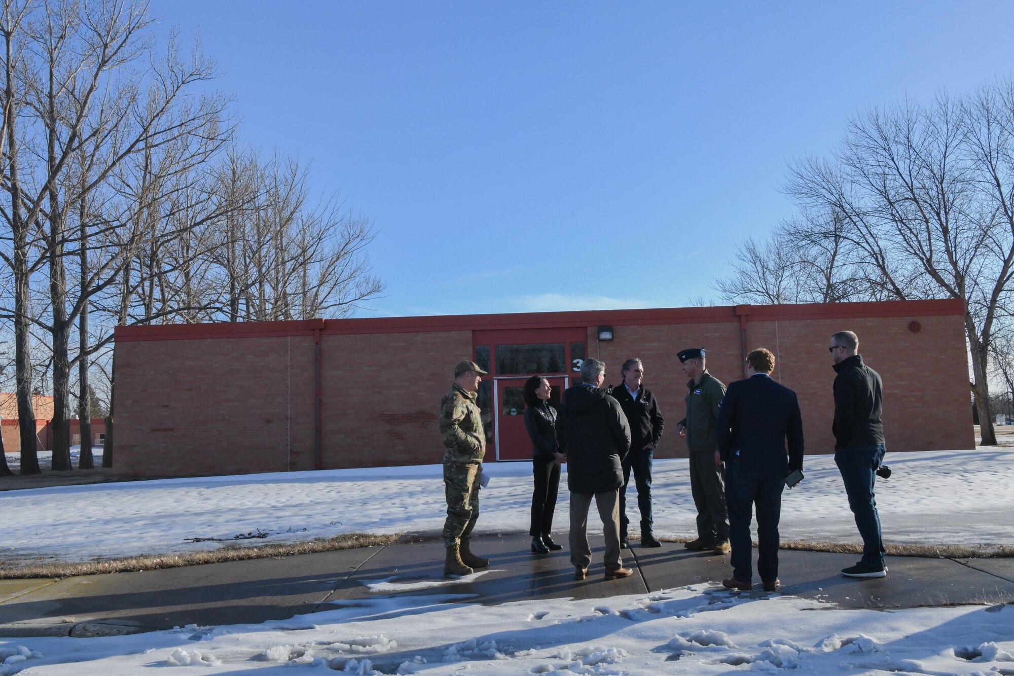 A group of people stand outside on a snow covered sidewalk in front of a school.