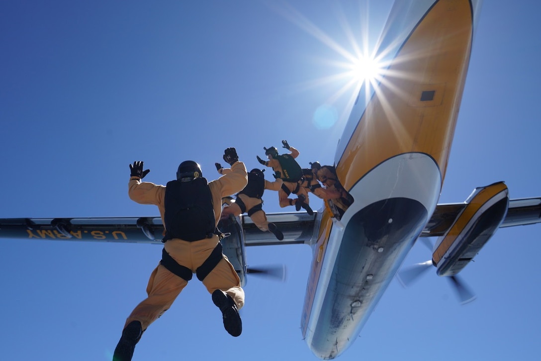 Soldiers jump out a yellow plane with their backs to the camera.