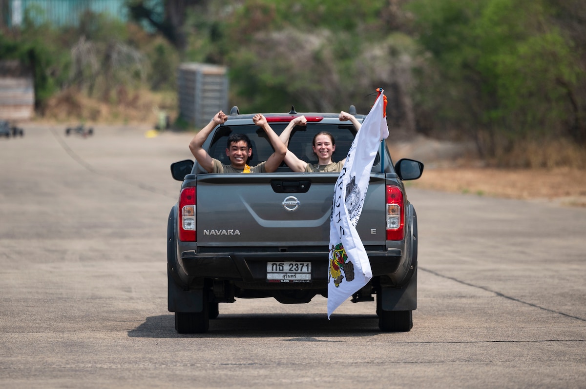 Airman 1st Class Darren Ky, left, and Senior Airman Ashley Taylor, both 80th Fighter Generation Squadron aircraft armament systems, perform a gesture of squadron pride while transitting to conduct maintenance on an F-16 Fighting Falcon