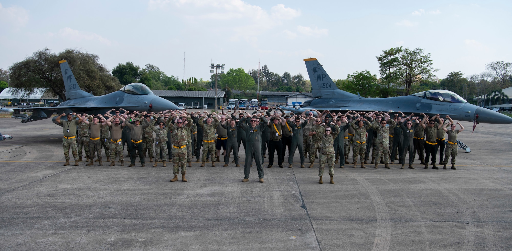 Airmen with the 80th Fighter Squadron and the 80th Fighter Generation Squadron strike a ‘Crush ‘Em’ pose for a group photo in front of two F-16 Fighting Falcons