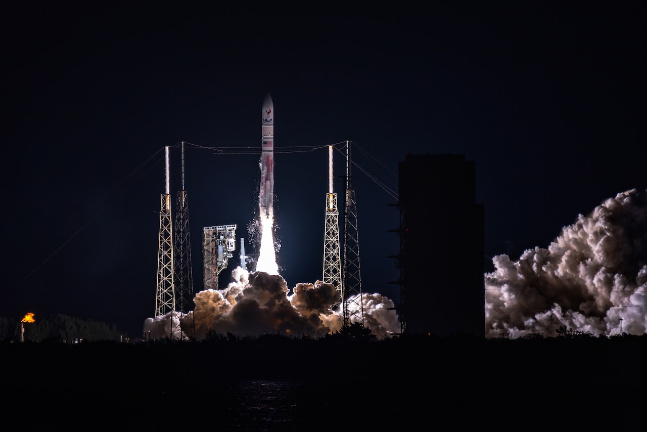 A rocket rises up from its launch pad at night with clouds of exhaust beneath it.