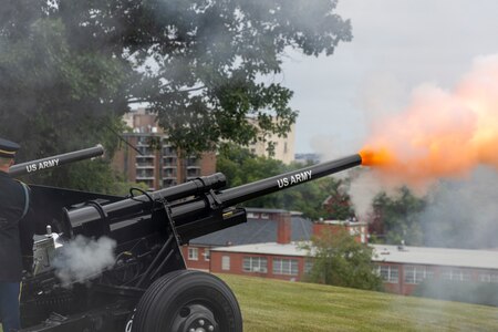 Black cannons that are placed on a green lawn are firing off with a plume of smoke and orange flame coming out of the end of the cannon barrel.