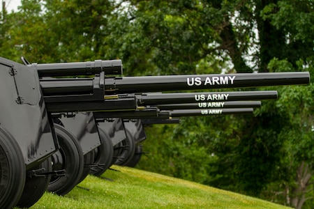 Several black cannons (on the left) with the words U.S. Army on the barrels are pointed out over a green lawn (on the right