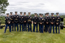 Army soldiers in dark ceremonial uniforms pose for picture in front of cannons that are placed on a green lawn.