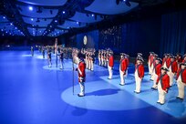Soldiers in various uniforms, including Revolutionary War-era red with blue trim and white pants, are standing in row (formations) along a wall in large room with spotlights shining on them.