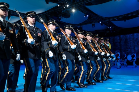 Army Soldiers in dark ceremonial uniforms are marching in rows (formation) with ceremonial rifles on their shoulders.