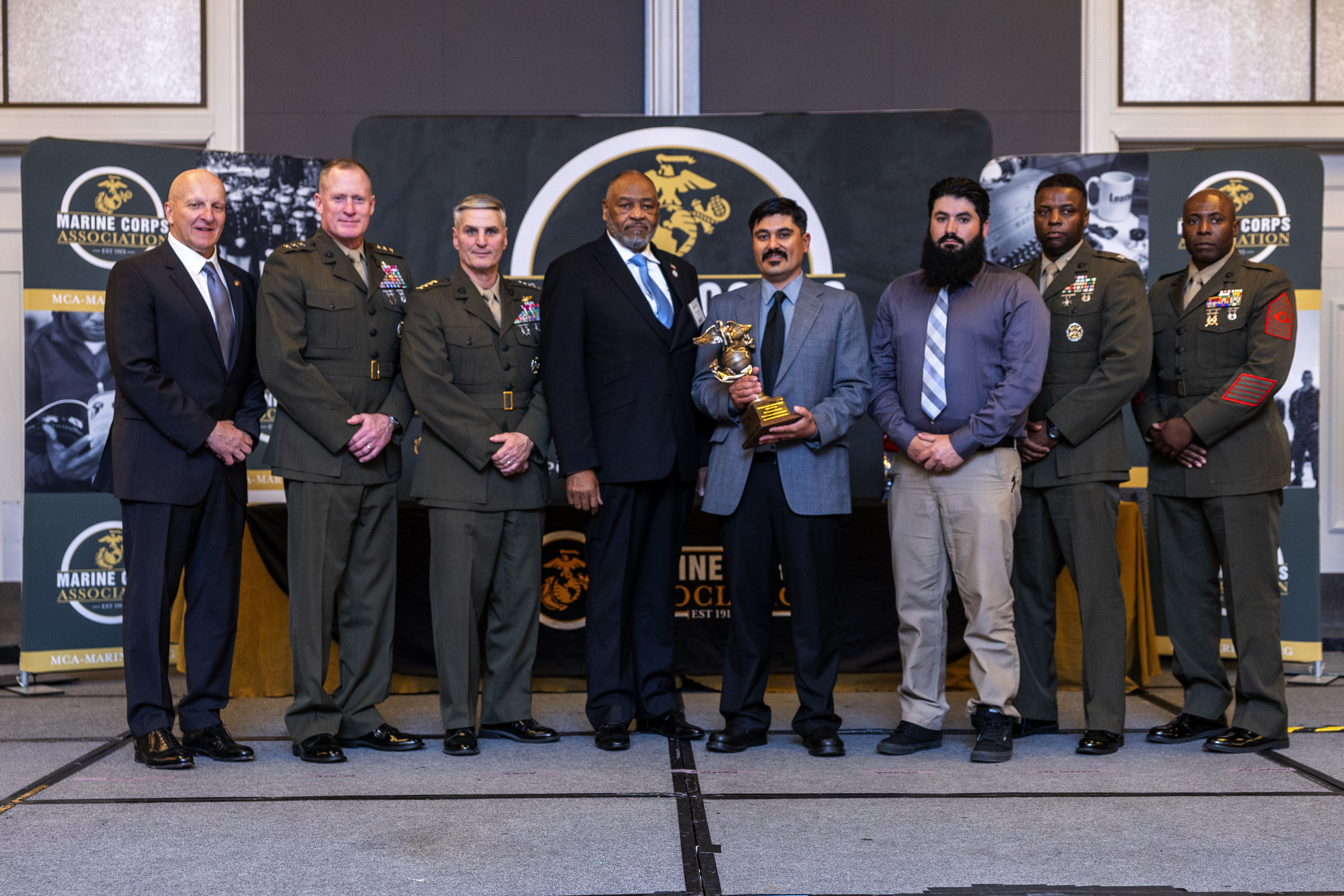 U.S. Marine Corps Gen. Christopher J. Mahoney, the Assistant Commandant of the Marine Corps, and Lt. Gen. Edward Banta, the Deputy Commandant of Installations and Logistics, presents an award to Mr. Lorenzo Zamora, the animal caretaker for Marine Corps Logistics Base Barstow, at the Hilton Alexandria Mark Center, Alexandria, VA on March 6, 2024. Zamora received the Marine Corps Installations Command Civilian of the Year award. (U.S. Marine Corps photo by Lance Cpl. Juaquin Greaves)