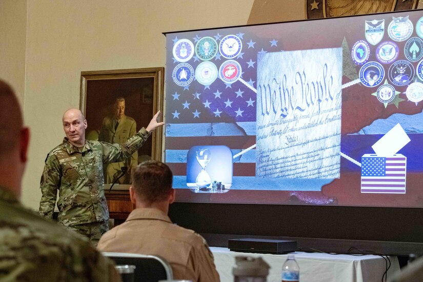 Air Force Chief of Staff Gen. David Allvin points at a projector with the Constitution, military branch logos and the American flag displayed with students seated before him.