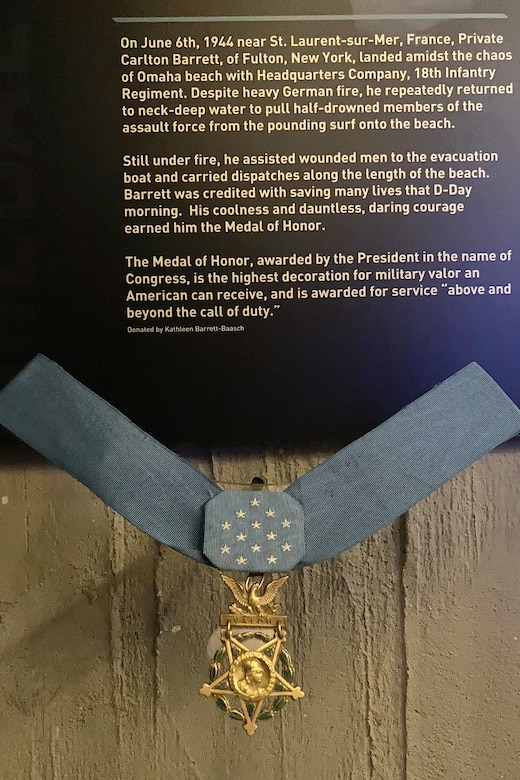 A medal hangs on a ribbon just below a plaque explaining who earned it.