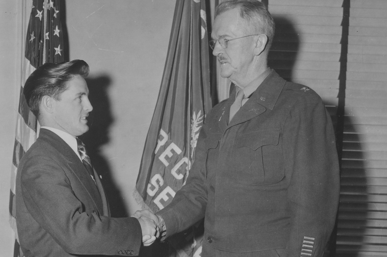 A person in business attire shakes hands with another person in a military uniform in this black and white photo.