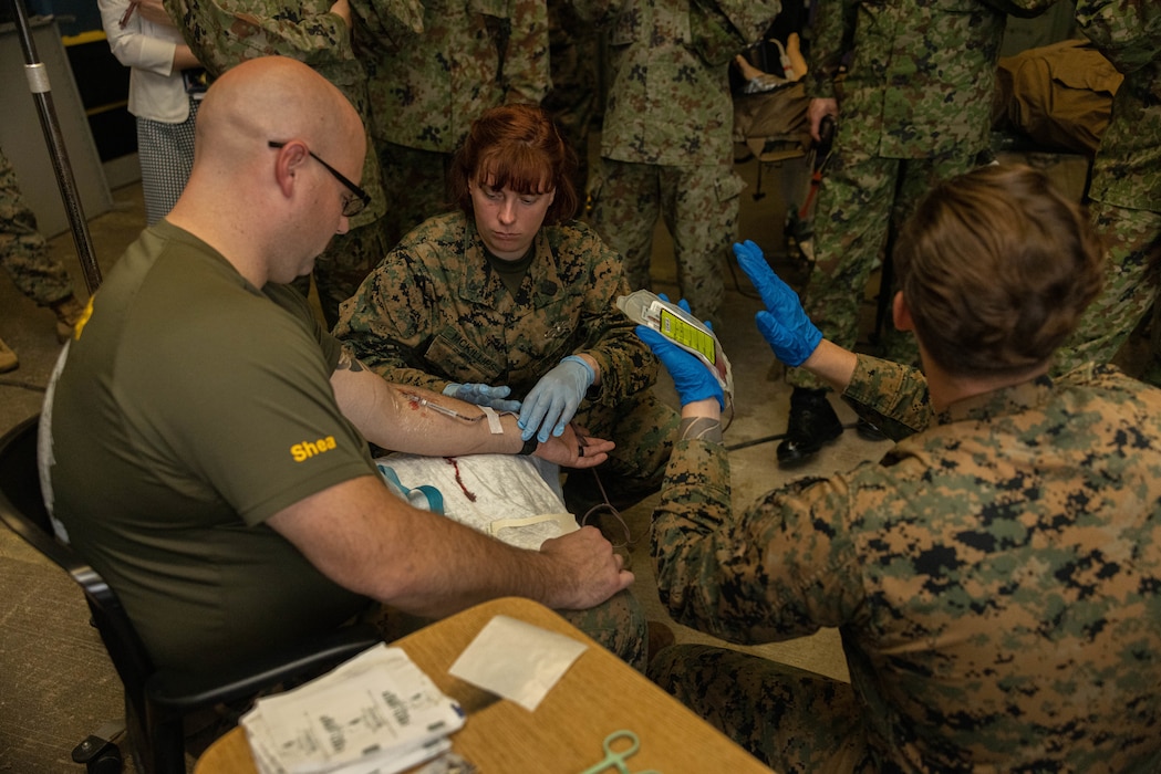 U.S. Navy Hospital Corpsman 3rd Class Abby Mckillips, middle, and Hospital Corpsman 3rd Class Matthew Barber, right, both Valkyrie instructors, demonstrate a blood transfusion on Navy Hospital Corpsman 3rd Class James Shea, left, a surgical technician, all with 3rd Medical Battalion, 3rd Marine Logistics Group at the Medical Skills Training Center, Camp Foster, Okinawa, Japan, Feb. 22, 2024. The blood transfusion training is part of the Valkyrie Program designed to train U.S. Navy Sailors and U.S. Marines in expeditionary blood transfusion. (U.S. Marine Corps photo by Lance Cpl. Weston Brown)