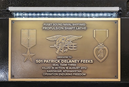 A plague honoring Special Warfare Operator 1st Class (Navy SEAL) Patrick D. Feeks is displayed prominently on a new propulsion shaft lathe inside Building 431, at Puget Sound Naval Shipyard & Intermediate Maintenance Facility in Bremerton, Washington. (U.S. Navy photo by Jeb Fach)