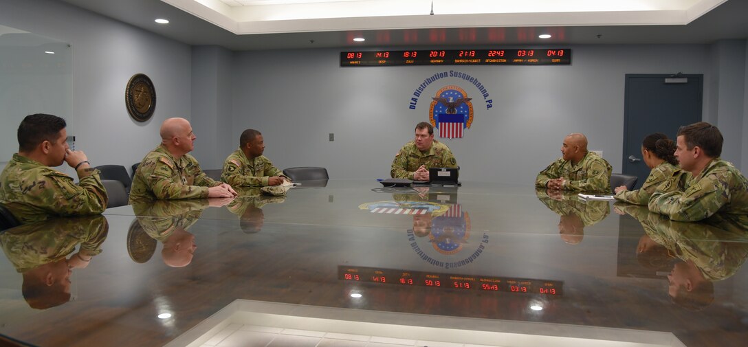 Photo is of a group of men in Army military uniform sitting around a large conference table.