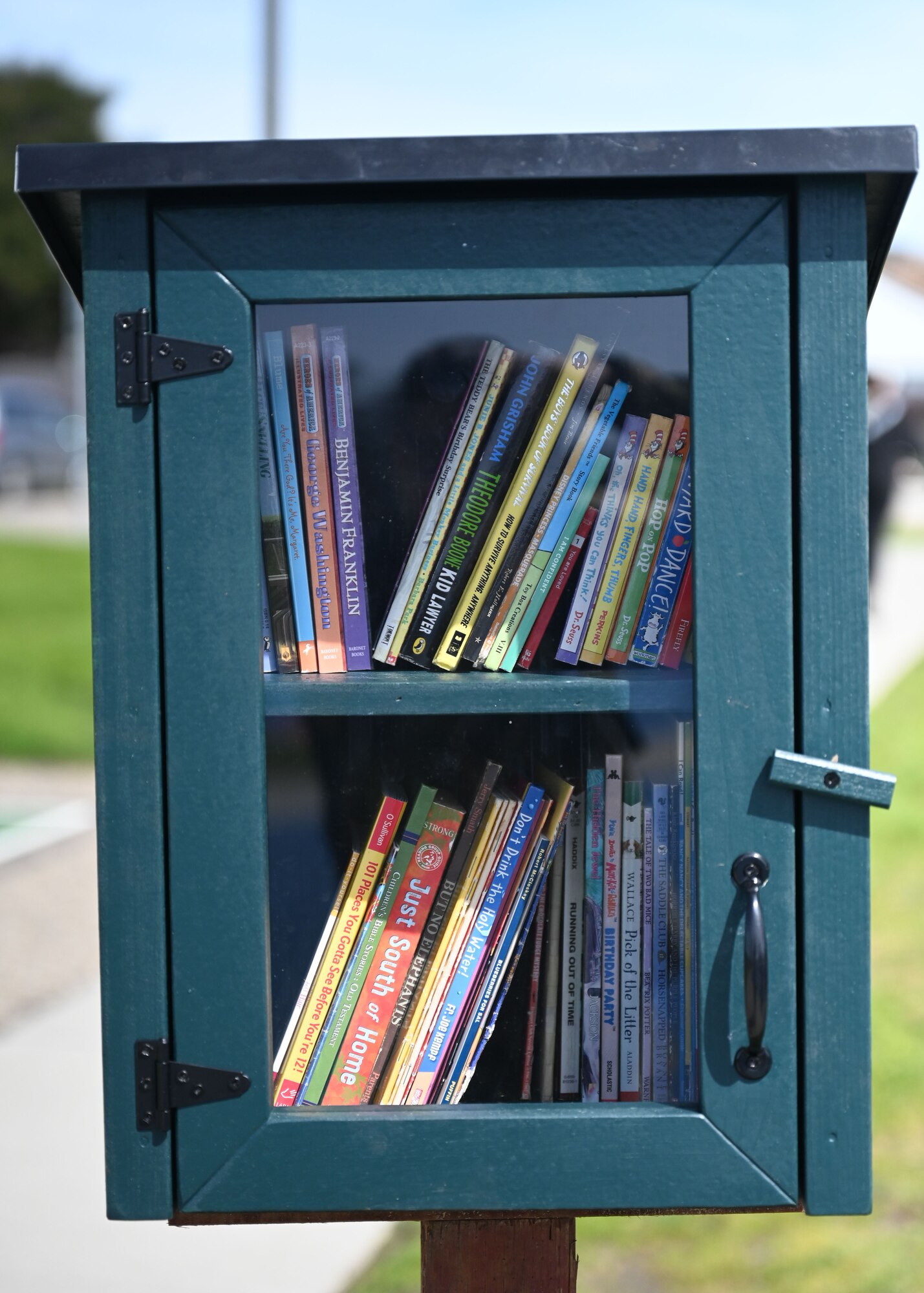 A photo of the little library, dark teal with windows showing books inside.