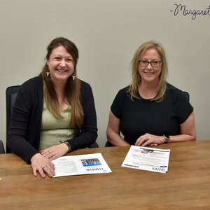 Two women sit at a table with papers.