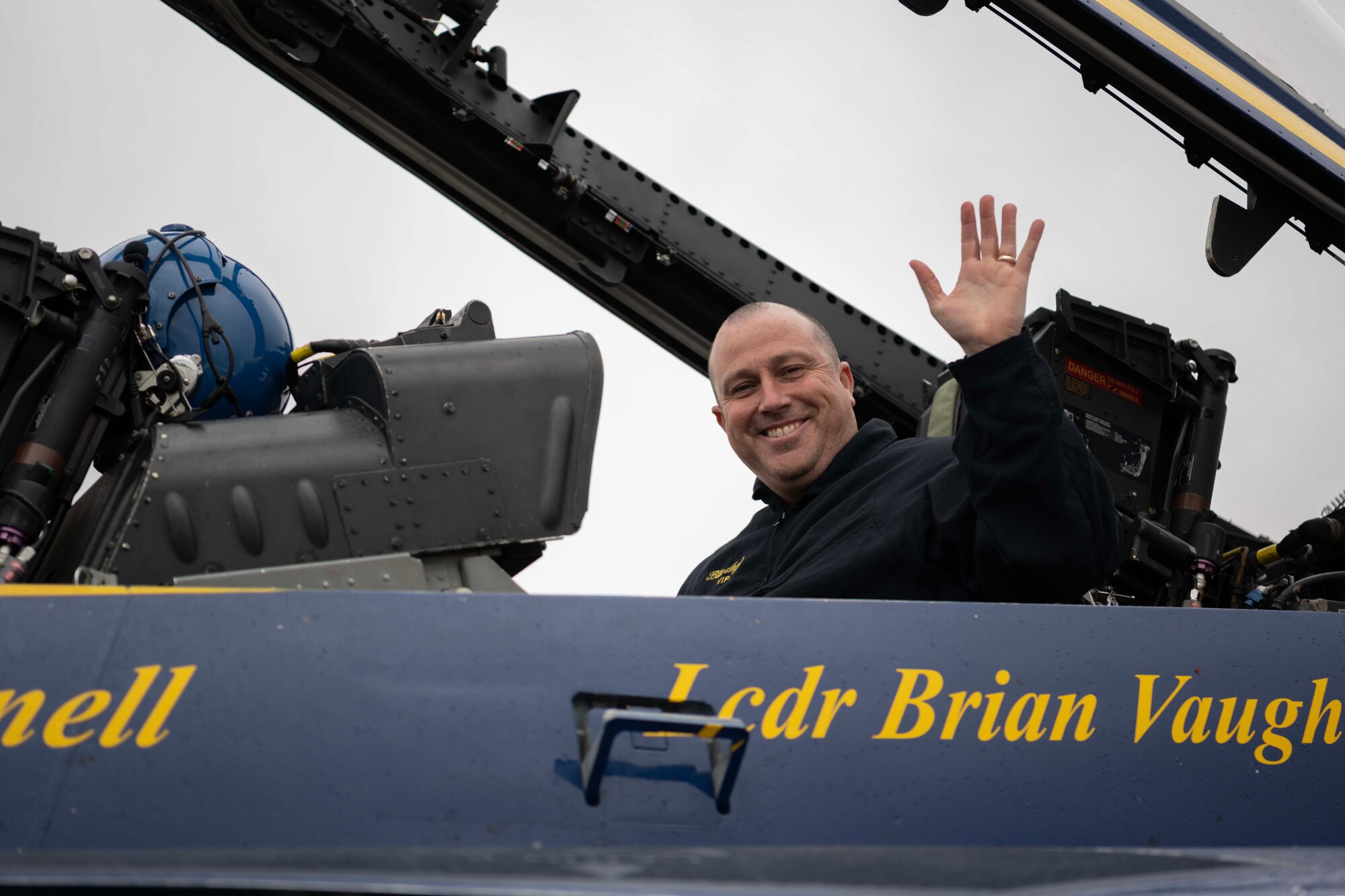 A man waves while sitting inside a military jet