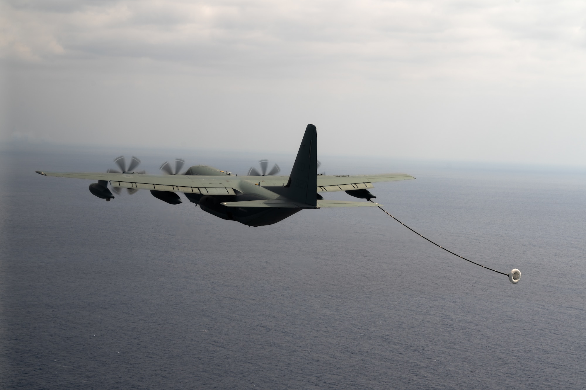 A cargo aircraft prepares to refuel helicopters in the air.