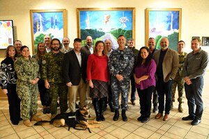 A group of 18 people and one dog stand together for a group photo inside the Pacific Coast Club entryway.