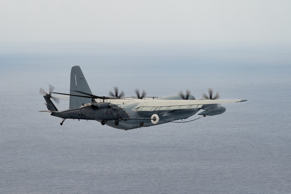 A cargo aircraft refuels a helicopter in the air.