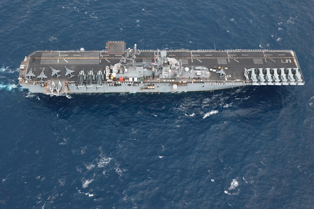 A large military ship steams across the ocean as seen from above.