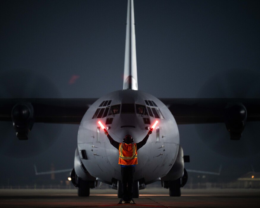 A U.S. Air Force maintainer marshals a U.S. C-130 Hercules on the flightline