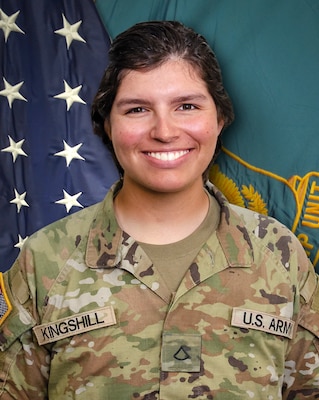 Woman in U.S. Army uniform standing in front of two flags.