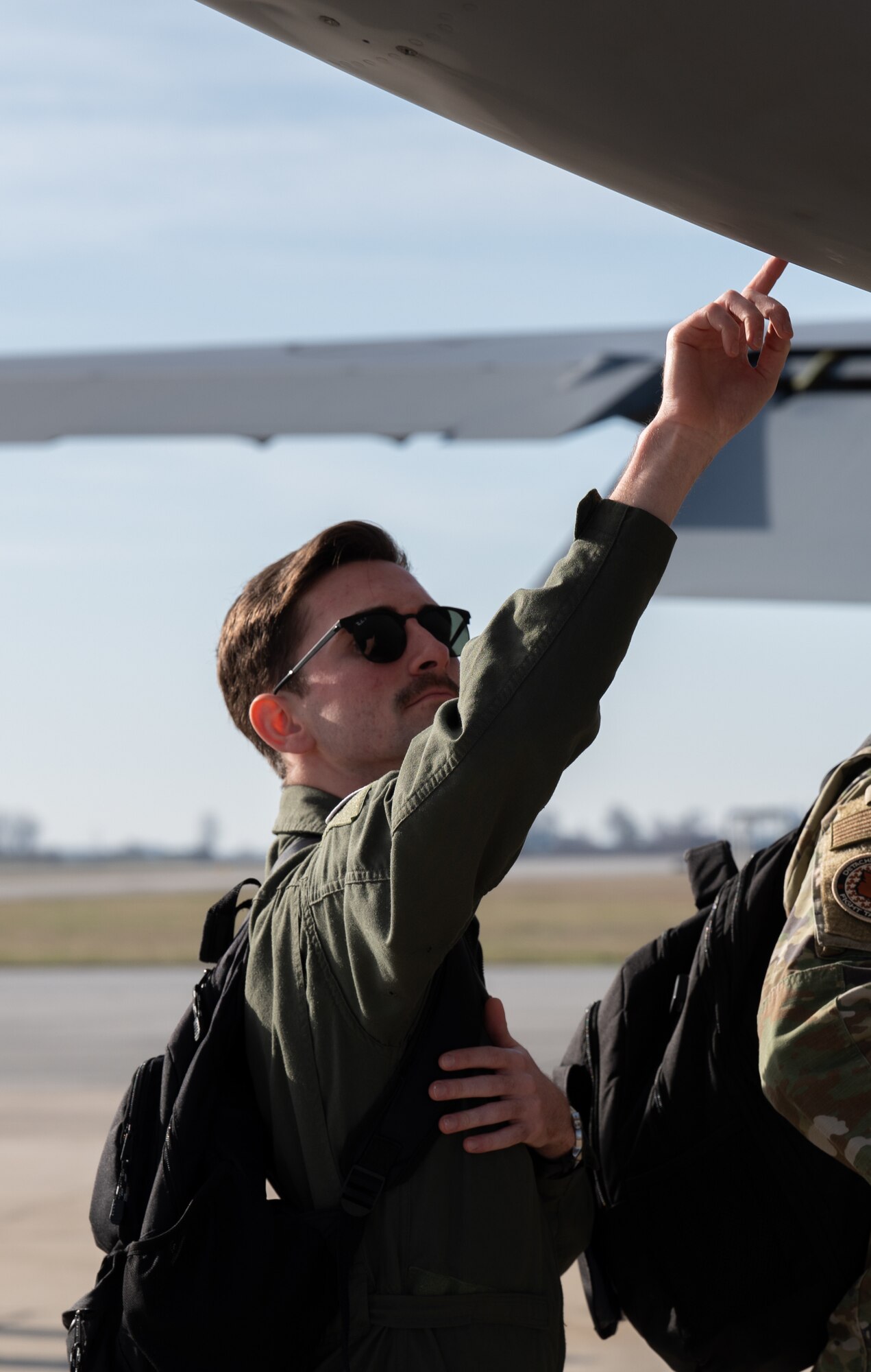 A man in a flight suit and glasses extends his hand to touch a gray, metallic object at the top right of the photo.