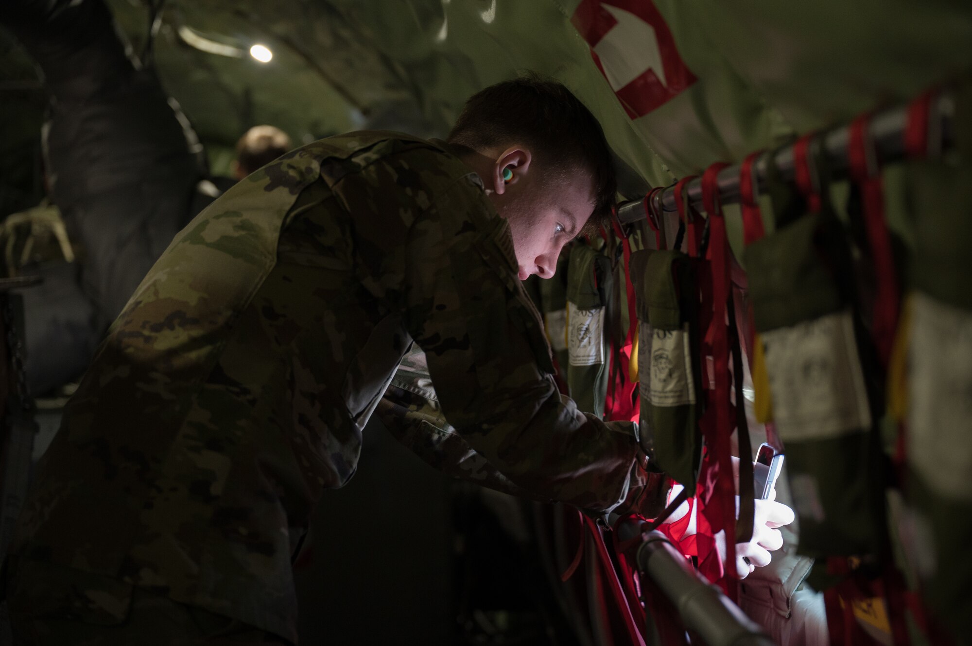 A man is seen, inside a military aircraft, taking a photo with his cell phone.