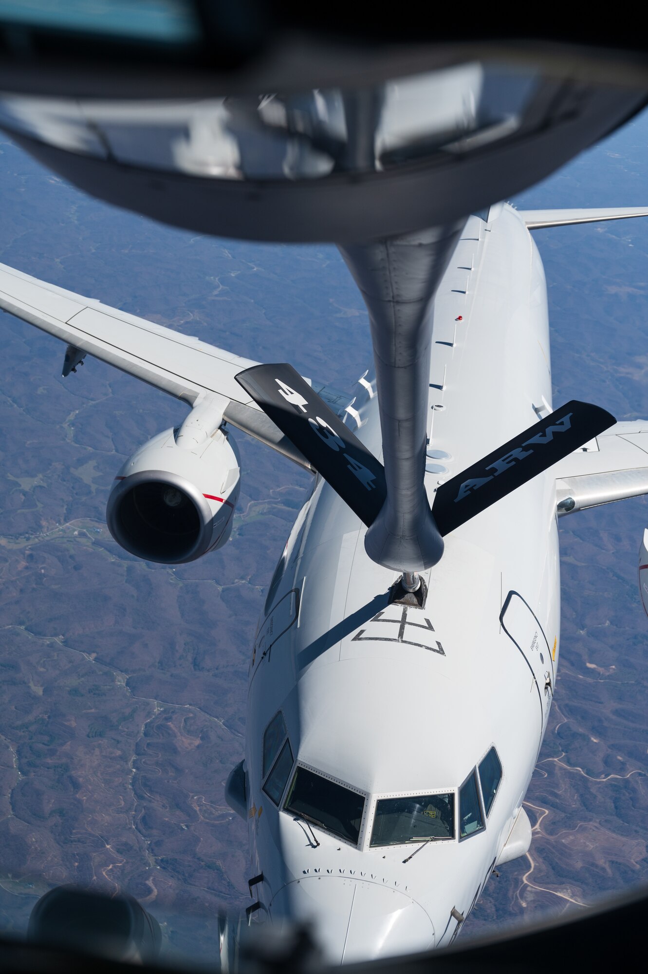 A white airplane, in flight, receives fuel from a fuel line that reads "434 ARW".