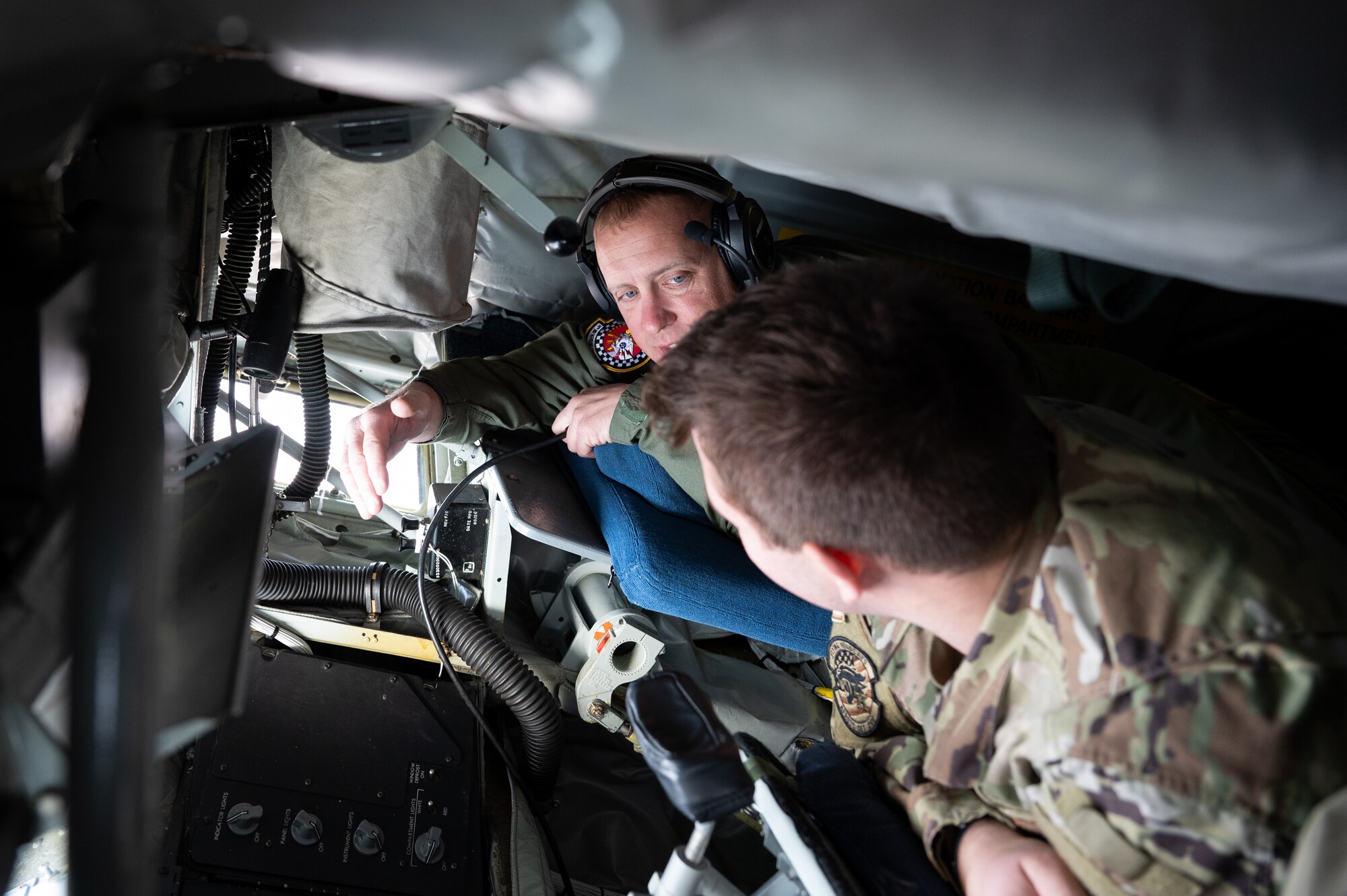 Two men are visible, seen talking to one another. Both are in military uniforms, laying on their stomachs in the boom pod of a KC-135.