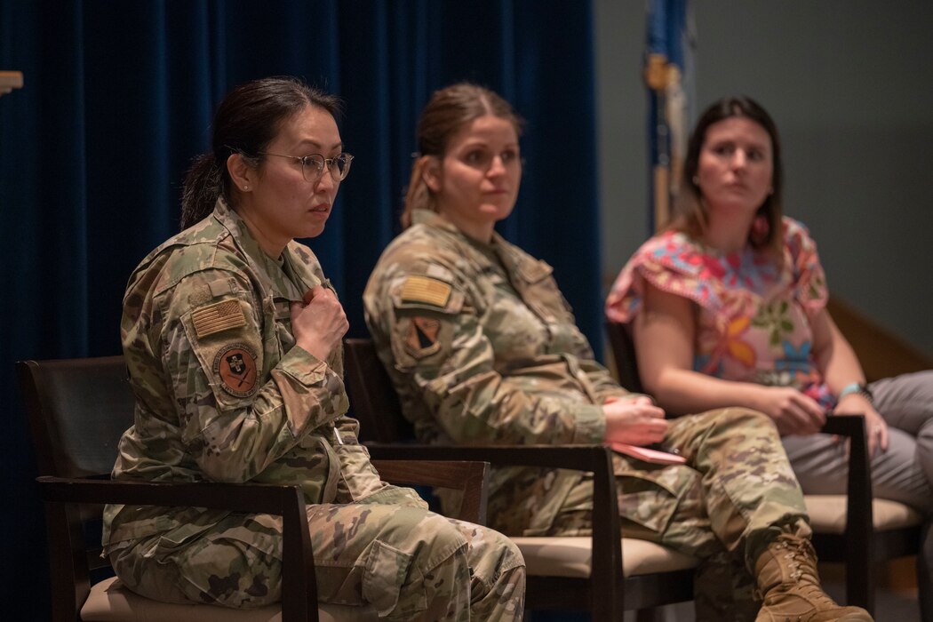 A woman with dark hair and glasses wearing a green military uniform speaks to an audience.