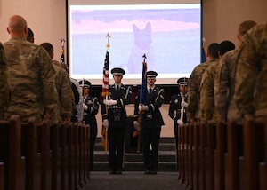 Four honor guard members in uniform hold flags in front of a crowd.