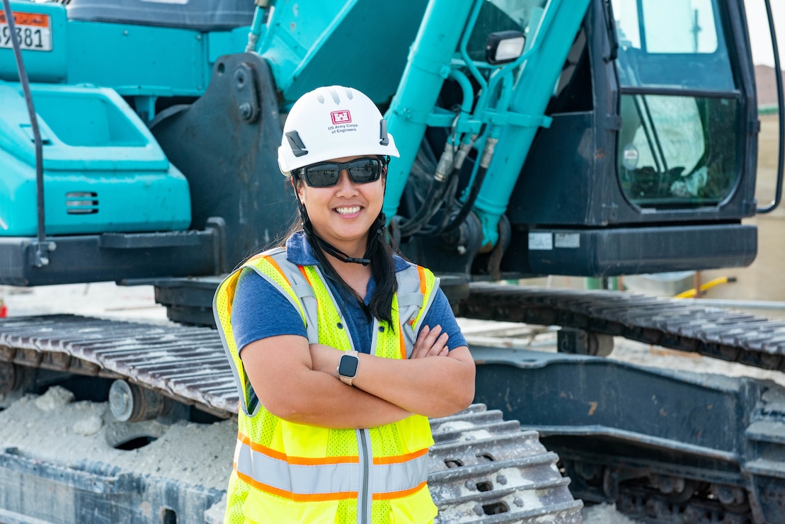 Woman in safety gear standing in front of heavy machinery,