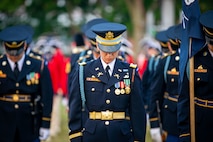 Soldiers standing up straight in rows (formation) are wearing dark ceremonial uniforms while looking down at the ground in front of them.