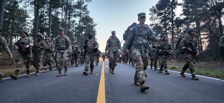 Soldiers in formation on the road being led by their female commanding officer.