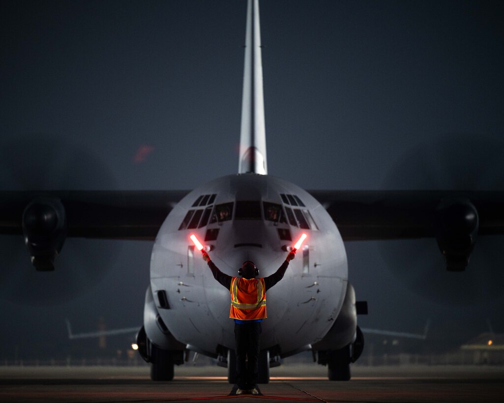 A U.S. Air Force maintainer marshals a U.S. C-130 Hercules on the flightline