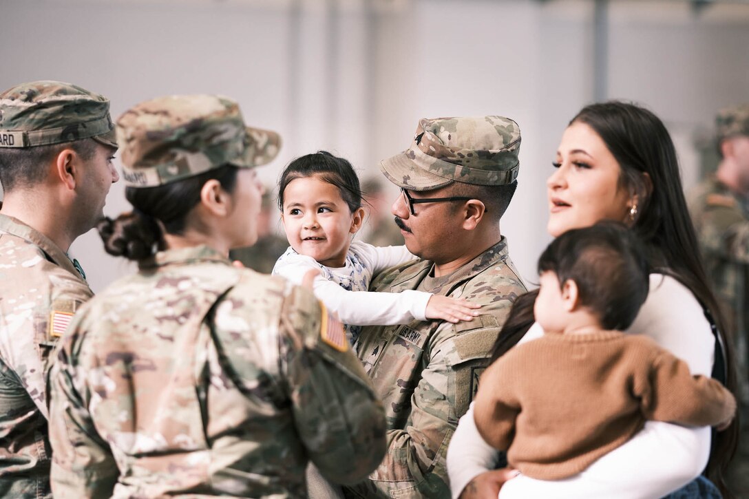 A soldier and a civilian each hold a child while engaging with two other soldiers.
